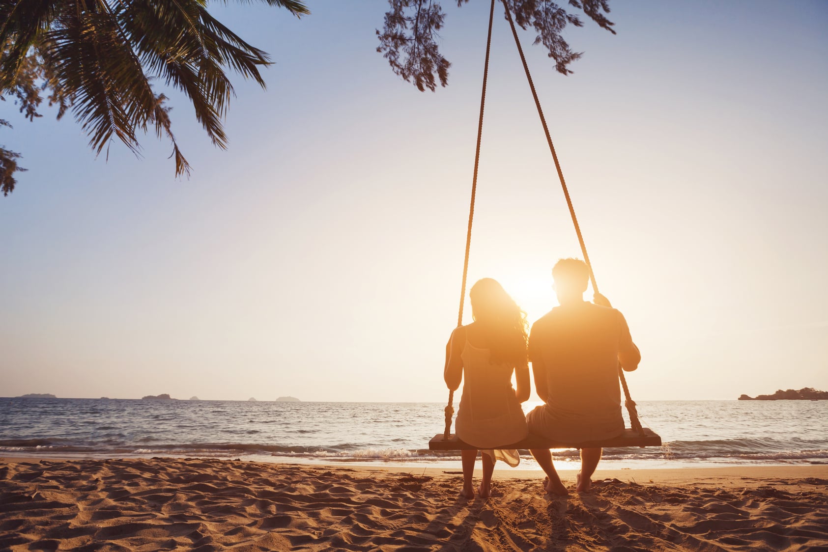 Couple on palm tree swing at sunset